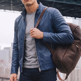 Men's blue faux leather biker jacket with quilted shoulders, three-quarter lifestyle view with shoulder bag