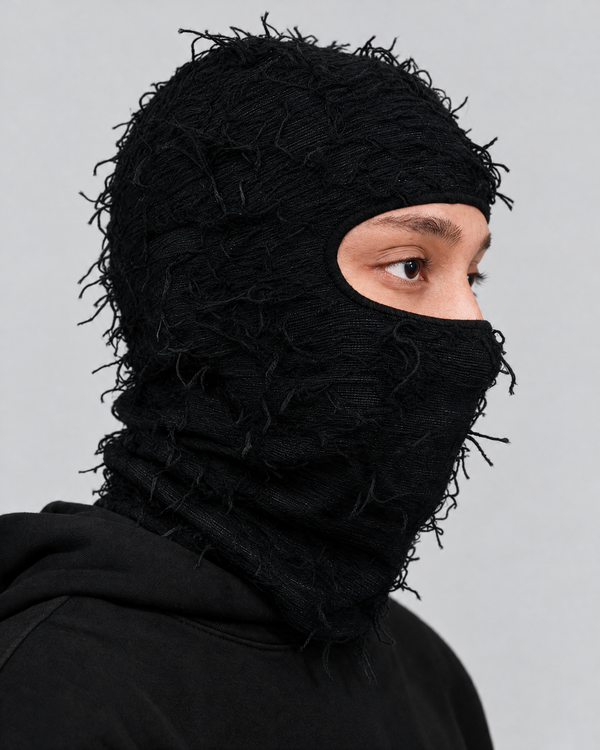 Black distressed knit balaclava on model against neutral light gray studio background