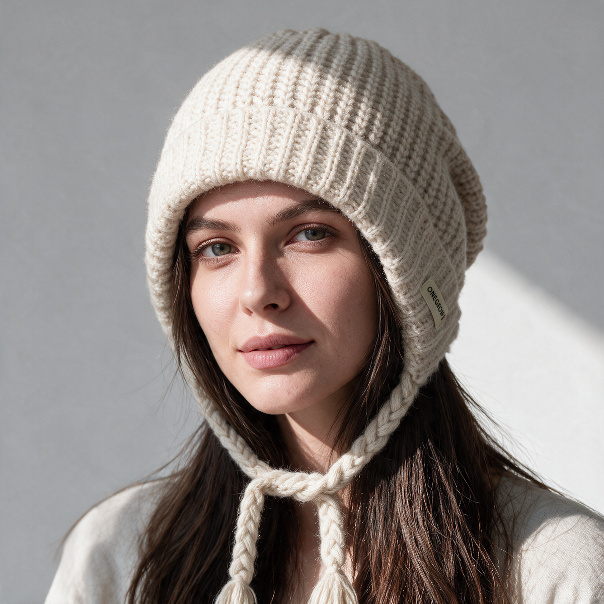 Cream knit earflap bonnet with braided ties worn in natural daylight